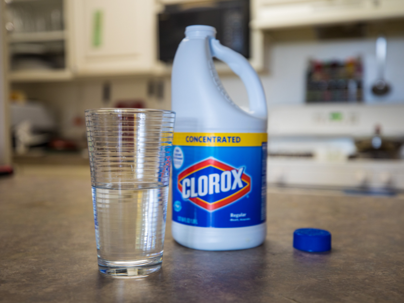 a bottle of bleach next to a glass of water on counter top